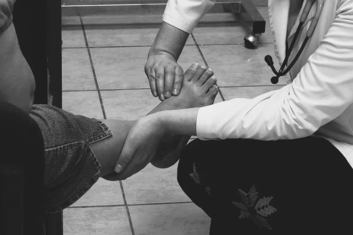 A clinician examines an adult patient’s foot and forefoot in a medical office.