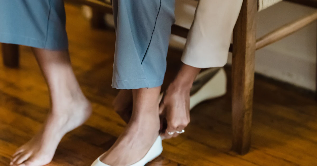 A woman in a bright home removes a walking shoe after feeling burning pain in the ball of her foot.