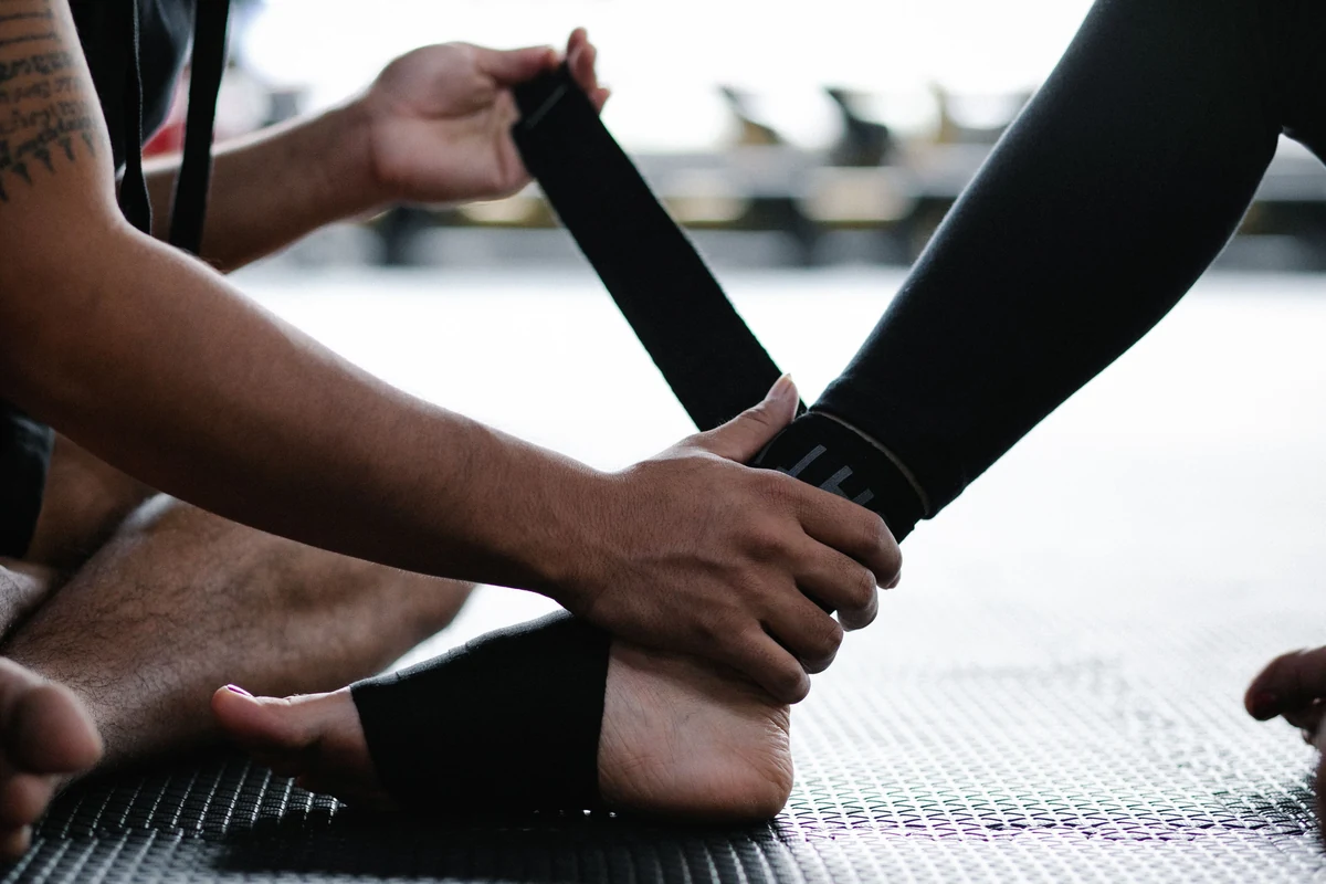 An adult athlete wraps an injured ankle with a supportive elastic bandage.